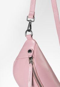 Roze leren handtas met een driehoekige vorm, voorzien van een ritssluiting aan de zijkant, een drukknoop en een stevige metalen clip voor de handtasstrap.