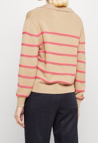 Beżowy sweter z dzianiny z różowymi poziomymi paskami, z kołnierzem i ściągaczami na rękawach. Projekt ma luźny krój i miękką fakturę.