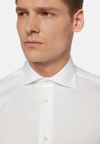 Weißes Hemd mit klassischem Kragen, das eine glatte Textur, dezenten Glanz und Einzelperlenknöpfe aufweist. Nahaufnahme von Kragen und Hals.