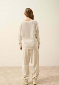 Sweter w kolorze kremowym, o fakturowanym, luźnym kroju, zestawiony z dopasowanymi spodniami szerokimi, widziany z tyłu, na neutralnym tle.