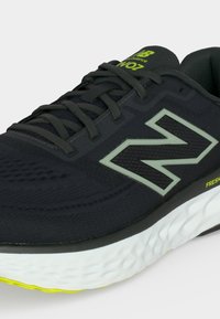 Μαύρο αθλητικό παπούτσι New Balance με λευκή σόλα, νέον κίτρινα σημεία και μεγάλο λογότυπο «N» στο πλάι, εμφανίζεται σε κοντινή λήψη.