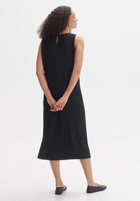 Black pleated dress with a sleeveless design, back keyhole detail, and a midi length, paired with simple black flats. Smooth texture.