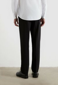 Czarne dopasowane spodnie o prostym kroju, wykonane z gładkiego materiału, w połączeniu z czarnymi skórzanymi butami. Częściowo widoczna biała koszula.