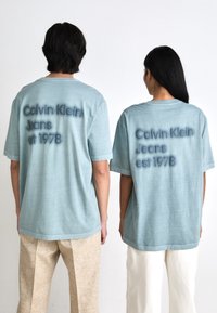 Vaaleansinisiä, ylisuuren kokoisia t-paitoja pehmeästä kankaasta, joissa on tummansinisellä tekstillä painatettuna "Calvin Klein Jeans est 1978" selässä.