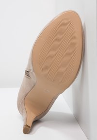 Tacón de ante beige con punta afilada. La suela es lisa y tiene un patrón en forma de ola para mayor tracción. Diseño minimalista con un sutil acento lateral.