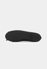 Sola de sapato preta com superfície lisa e ligeira curvatura, apresentando logótipo da marca em relevo e detalhes de tamanho. Design minimalista.