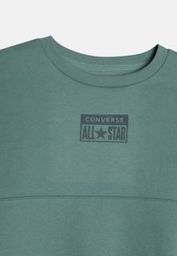 Zielona bluza z okrągłym dekoltem, z wytłoczonym na klatce piersiowej granatowym logo "Converse All Star" oraz kontrastowymi szwami.