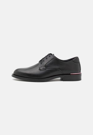 Chaussure habillée en cuir noir à finition lisse, bout arrondi et cinq œillets pour les lacets. Présente un accent de couleur discret sur le talon.