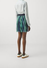 Ljusblå skjorta med baksidan i yoke-stil, i kombination med en grön och blå mönstrad kjol, samt vita sneakers med grön accentsfärg och gummisulor.