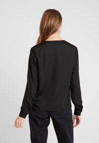 Svart långärmad topp med en mjuk, svagt glansig yta, rundad halsringning och avslappnad passform, som är kombinerad med mörka jeans.