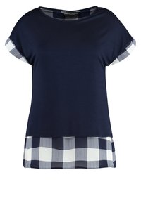 Mörkblå topp med korta ärmar, med en rutigt fåll i vitt och mörkblått, tillverkad av ett lätt tyg för en lager-på-lager-look.