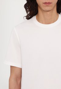 White cotton t-shirt with a round neckline and short sleeves, featuring a smooth texture and minimalistic design. No patterns or accents.