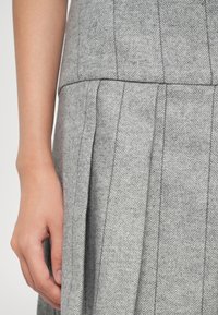 Tessuto grigio a zig-zag con pieghe verticali, che mostra un primo piano di una mano appoggiata sul materiale texturizzato.