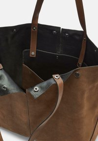 Bruine en zwarte lederen tote bag met dubbele handvatten en drukknoopsluitingen, met zichtbare binnenzakken en steekdetails.