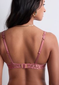 Un soutien-gorge en dentelle rose présente un motif floral, des bretelles en satin et une fermeture par agrafe. Le dos met en valeur un design lisse et texturé.