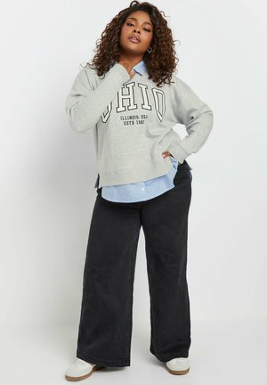 Hellgrau Sweatshirt mit "OHIO"-Schriftzug, getragen über einem blau-weiß gestreiften Hemd mit Kragen. Kombiniert mit weit geschnittenen schwarzen Hosen und weißen Schuhen.