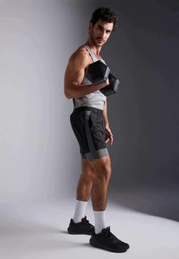 Juodas hantelis, pilkas sportinis marškinėliai ir šortai su šoninėmis juostelėmis. Modelis pozavo su rimtu išraiška, vilkėdamas juodus sportbačius ir baltas kojines.
