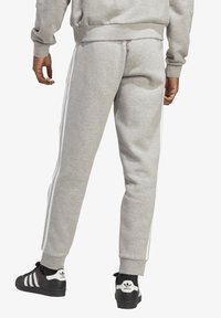 Sive bombažne jogger hlače z elastičnimi manšeti, ki imajo bele stranske črte. V kombinaciji s črnimi supergami in rebrastimi nogavicami do gležnjev.