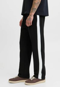Sorte sweatpants med en hvid sidestribe, lavet af blødt materiale. Har en afslappet pasform og ribbede manchetter. Kombineret med brune sneakers.