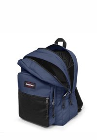 Blå tygryggsäck med flera fack, framfack i svart nät, dragkedjor och ett handtag på toppen för bärande.