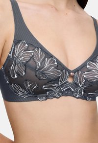 Melna un balta ziedu mežģīņu krūšturis uz sievietes torša ar mazu rozā zelta piekariņu centrā.