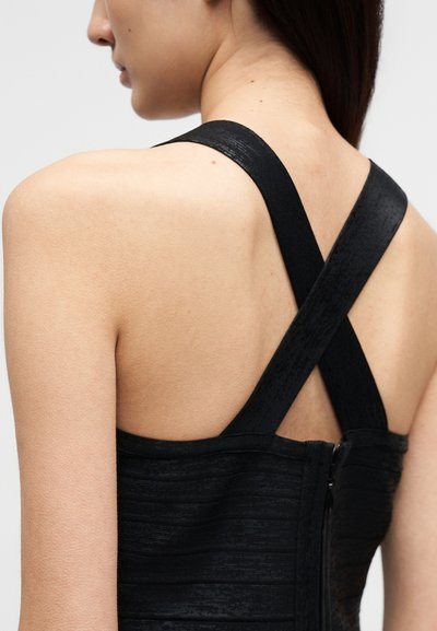 Μαύρο αμάνικο φόρεμα με υφή, με φαρδιές, σταυρωτές τιράντες στους ώμους και λεπτομέρεια φερμουάρ στο πίσω μέρος.