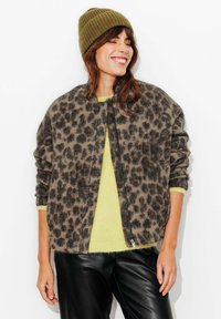 Veste bomber duveteuse à imprimé léopard marron et noir, associée à un pull jaune vif et à un pantalon en cuir noir. Bonnet en maille vert olive.
