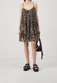 Vestido sin mangas en estampado de cebra negro y beige, hecho de una tela ligera. Combinado con sandalias negras gruesas y un bolso negro pequeño.