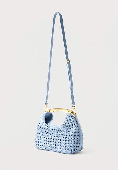 Τσάντα ώμου από φωτεινό γαλάζιο υφαντό δέρμα με λαβή σε χρυσό τόνο με καμπύλη και ρυθμιζόμενο ιμάντα ώμου, κρεμασμένη σε απλό φόντο.