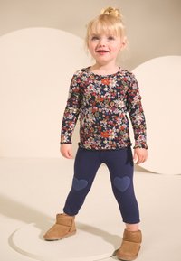 Bluza cu mâneci lungi în culoarea bleumarin, decorată cu flori și manșete cu volane, combinată cu colanți bleumarin cu accente în formă de inimă pe genunchi și cizme scurte bej.