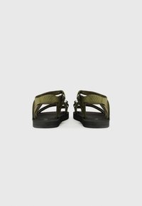 Grønn sandal med bred stroppdesign, justerbare stropper og flat svart gummisåle. Minimalistisk konstruksjon uten intrikate mønstre.