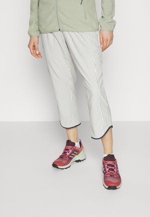 Ανοιχτό πράσινο ζακέτα με φερμουάρ, λευκό και ναυτικό μπλε ριγέ ψηλόμεσες παντελόνες και ροζ και μωβ αθλητικά παπούτσια με μαύρες σόλες.