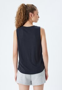 Zwarte mouwloze top met een ronde zoom, zachte textuur en minimaal ontwerp. Gecombineerd met lichtgrijze shorts, heeft een eenvoudige esthetiek.