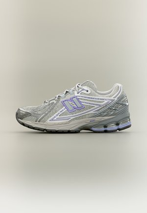 Grauer und lavendelfarbener New Balance Laufschuh mit Mesh-Gewebe, gepolsterter Sohle und Schnürdesign vor neutralem Hintergrund.