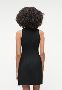 Čierne bezrukávové šaty s priliehavým strihom, so hladkou textúrou a jemným švom pozdĺž chrbta.