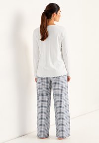Vit ribbad långärmad topp i kombination med löst sittande pyjamasbyxor i blå och vita rutor, med fransad nederkant och sidfickor.