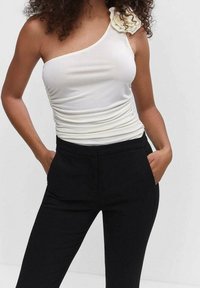 Haut blanc à une épaule avec une texture froncée et un accent en fleur en tissu ; associé à un pantalon noir ajusté.