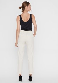 Pantaloni beige chiari a sigaretta con vita elasticizzata e tasche posteriori, abbinati a un top senza maniche nero e tacchi neri.