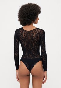 Body in pizzo nero con maniche lunghe, caratterizzato da intricate fantasie floreali e taglio a perizoma. Tessuto morbido con un design trasparente sulla schiena.