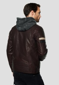 Pánska bordová kožená bunda s odnímateľnou sivou kapucňou, rebrovanými akcentmi na ramenách a kontrastnými pruhmi na rukávoch. Hladká textúra.
