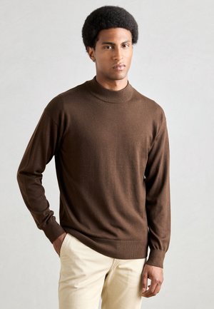 Brown lange mouwen turtleneck sweater van een zachte brei-stof, met een aansluitend ontwerp en geribde manchetten, gecombineerd met lichtbeige broeken.