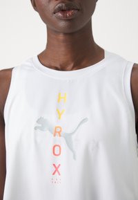 Biała bezrękawnikowa koszulka sportowa z gradientowym nadrukiem "HYROX" w odcieniach żółtego, pomarańczowego i różowego, z szarym sylwetką biegnącej pantery.