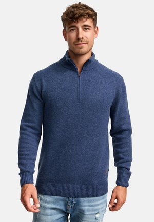 Granatowy sweter z dzianiny z kołnierzem na ćwierć zamka, prążkowanymi mankietami i dołem, teksturowana tkanina, w zestawieniu z jasnoniebieskimi, przetartymi dżinsami.