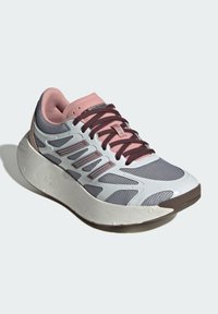 Scarpa sportiva grigia e rosa con tomaia in rete, sovrapposizioni testurizzate, lacci bordeaux e una suola bianca spessa. Accenti di design notevoli sui lati.
