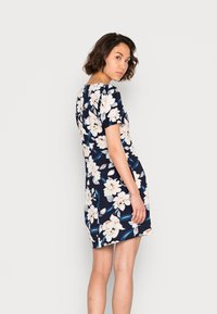 Vestido floral em tecido azul marinho com mangas curtas. Apresenta flores brancas e rosas, folhas verdes e uma forma ajustada que termina acima do joelho.