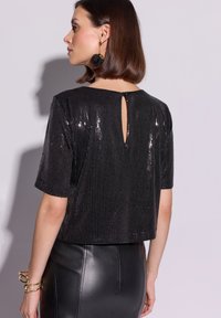 Czarny krótki top z cekinami, krótkimi rękawami, detalem z wycięciem na plecach i gładką fakturą materiału, zestawiony z ołówkową spódnicą z wysokim stanem.