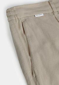 Pantalon beige texturé avec une ceinture élastique et une poche latérale, portant une petite étiquette blanche indiquant "MR MARVIS" près de la taille.