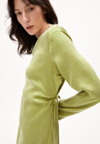 Grünes Leinenkleid mit langen Ärmeln, einem Bindeband in der Taille und einer glatten, leicht strukturierten Oberfläche.