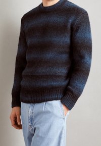 Maglione a righe blu e nere in maglia con scollatura a girocollo e orlo a coste, abbinato a jeans azzurri chiari. Tessuto in lana testurizzato.