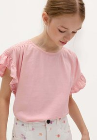 Helles rosa T-Shirt mit kurzen Rü scheln und einem Rundhalsausschnitt, aus weichem Stoff gefertigt. Kombiniert mit gemusterten, pastellfarbenen Shorts.